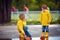 Cute boys, brothers having fun together, launching the paper boats in spring puddles, wearing raincoats and rubber boots