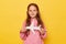 Cute brown haired positive little girl wearing pink sweatshirt holding white paper plane isolated over yellow background looking