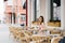 Cute brown-haired young girl sitting in a cafe outdoor; rattan chairs. The guy is late for a date the Girl is waiting