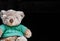 Cute brown teddy bear put green shirt on black background