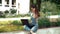 Cute brunette in jeans jumpsuit sitting on the street and looking at laptop