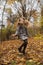 Cute brunette teen girl in gray coat jumps in the autumly forest . Cosiness, autumn, fun