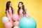 Cute brunette twins in pink dresses over yellow background.