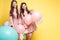 Cute brunette twins in pink dresses over yellow background.