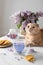 Cute cat, a cup of purple tea and a bouquet of blooming lilac on a light background. Spring tea drinking. Greeting card,
