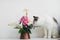 Cute cat smelling summer flowers bouquet in vintage vase on white  table. Home decor and pet. Curious kitty playing at stylish