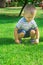 Cute Caucasian Blond Baby Boy with Blue Eyes Toddler of 2 Years Old Sits on Haunches on Green Grass