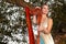 Cute Caucasian Blond Girl in Long Dress Playing the Harp on tree Branch on Park Outdoors