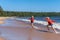 Cute caucasian boys wearing red hoodies and blue underpants running from waves in Ladoga lake with enthusiasm.