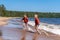 Cute caucasian boys wearing red hoodies and blue underpants running from waves in Ladoga lake with enthusiasm.