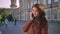 Cute caucasian brunette girl is standing near antiend building and talking over phone with gorgeous smile and happy look