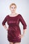 Cute caucasian curvy girl with short blonde hair and plus size body wearing beautiful elegant cherry color dress with sequins and