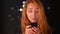 Cute caucasian ginger girl is holding her phone and looking at screen concentrated with focused beautiful face, artistic