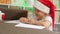 cute caucasian girl 5-6 years old in a santa hat writes a letter to santa claus