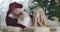 Cute Caucasian girl with blond curly hair lying with Santa at the background of Christmas tree and smiling. Pretty child