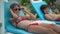 Cute Caucasian tanned girl putting on sunglasses looking at camera smiling sunbathing with brother at summer resort