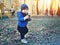 Cute caucasian toddler boy in casual clothes walking in city park holding paper cup and sipping warm drink. Adorable child having