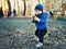 Cute caucasian toddler boy in casual clothes walking in city park holding paper cup and sipping warm drink. Adorable child having