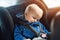 Cute caucasian toddler boy sleeping in child safety seat in car during road trip. Adorable baby dreaming asleep in comfortable