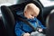 Cute caucasian toodler boy sleeping in child safety seat in car during road trip. Adorable baby dreaming asleep in comfortable