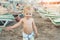 Cute caucasian toodler boy walking alone on sandy beach between chaise-lounge. Adorable happy child having fun playing at seaside