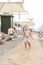 Cute caucasian toodler boy walking alone on sandy beach between chaise-lounge. Adorable happy child having fun playing at seaside