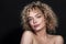 Cute caucasian woman with afro curls hairstyle on a dark background. She wears nude make up