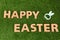 Cute ceramic bunny ears and text HAPPY EASTER made of wooden letters on green grass