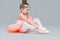 Cute charming ballerina little girl in pink tutu is sitting on the floor trying to put on ballet shoes