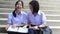 Cute cheerful Asian Thai high schoolgirls student couple in school uniform sit on the stairway having a fun discussing homework