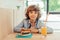 cute cheerful curly boy sitting in cafe in cafe with piece of cake