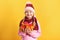 Cute cheerful little girl with an armful of autumn maple leaves. Child in hat and scarf on a yellow background