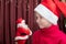 A cute cheerful little girl in a Christmas red cap asks a toy Santa Claus for gifts. Happy New Year and Christmas