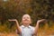 Cute cheerful little girl stands in the rain in the autumn park. The child held out his hands and collects drops in the palm of