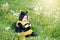 cute and cheerful portrait of little child sitting in blooming flowers of dandelion in yellow bee costume