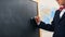 Cute cheerful schoolboy writes on the blackboard with chalk. Copy space