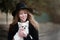 Cute cheerful slim caucasian girl blonde with long hair in a black coat and a black hat in in the autumn day with her white small
