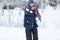 Cute, cheerful young boy in hat, blue jacket plays with snow, has fun, smiles, makes snowman in winter park.