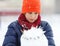 Cute, cheerful young boy in hat, blue jacket plays with snow, has fun, smiles, makes snowman in winter park.