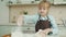 Cute child blond girl in apron cooking in kitchen mixing dough adding flour making pastry