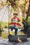 Cute child, boy in colorful jacket, playing with boat and ducks on a little river, sailing and boating. Kid having fun, childhood