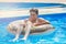 Cute child boy on funny inflatable donut float ring in swimming pool with oranges. Teenager learning to swim,