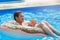 Cute child boy on funny inflatable donut float ring in swimming pool with oranges. Teenager learning to swim, have fun in outdoor