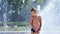 Cute child, a boy of seven years having fun, bathes in a fountain and playing water splash in outside, on a hot summer
