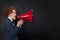 Cute child boy speaking through a megaphone against a blackboard with copy space. Kid with loudspeaker