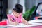 Cute child doing artwork on red desk. Asian girl drawing cartoon on paper. Happy kid learning at home. Children aged 4 years old
