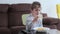 Cute child eating macaroni with tomato sauce and parmesan using the fork while watching TV at home.