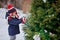 Cute child girl in christmas knitted hat decorating tree in winter snowy garden