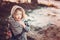 Cute child girl in grey knitted coat plays on the walk in winter forest