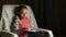 Cute child girl in grey pink sweatshirt sits in comfortable chair in room and reads book